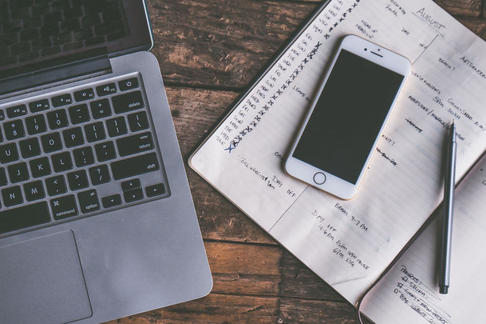 A laptop and phone next to a handwritten weekly schedule planner