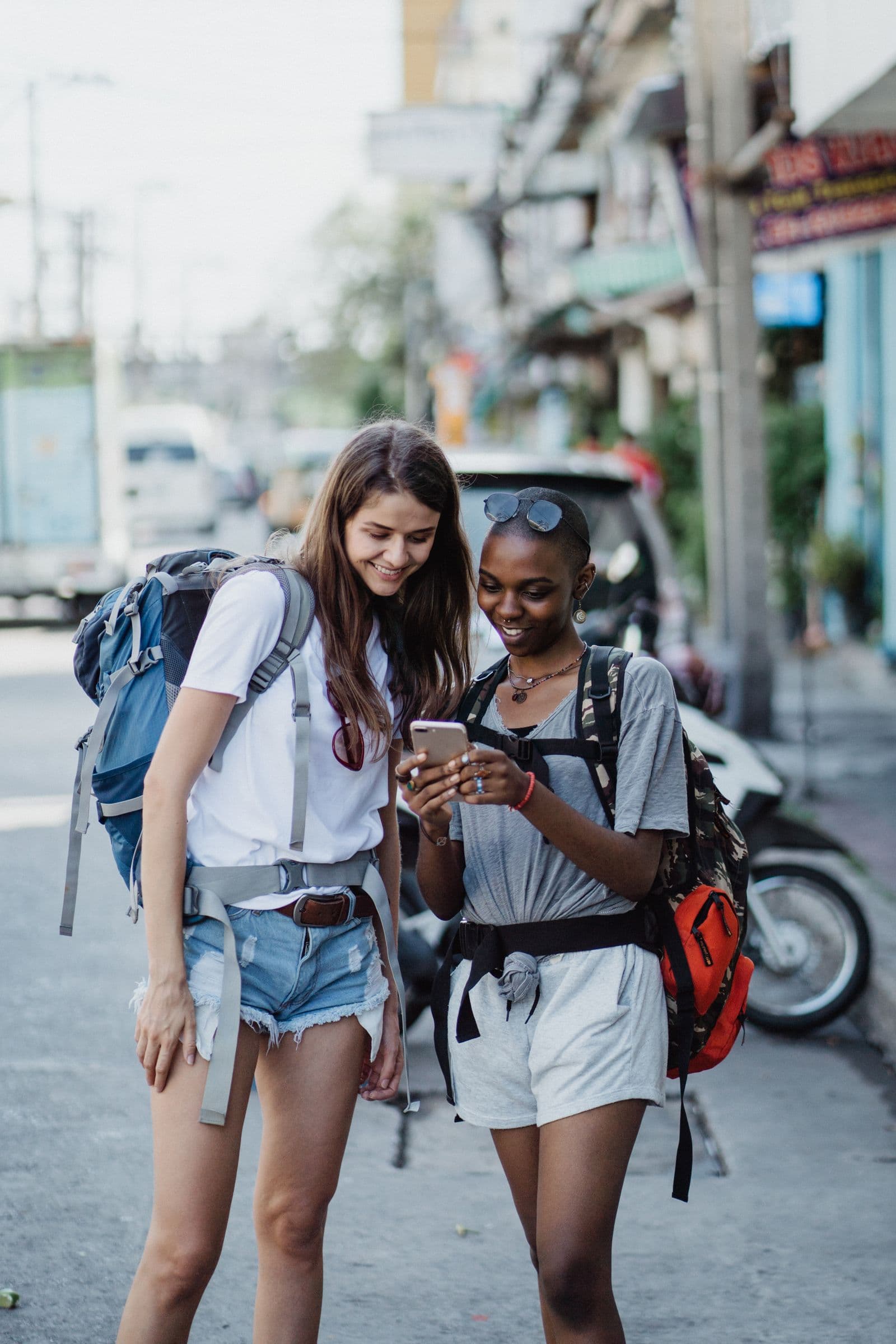 Two travelers with backpacks looking at a phone together on a city street